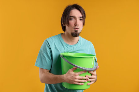 Man with bucket suffering from nausea on yellow backgroundの写真素材