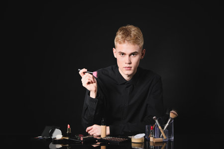 Makeup artist with tools and cosmetic products at table on black background. Space for textの写真素材
