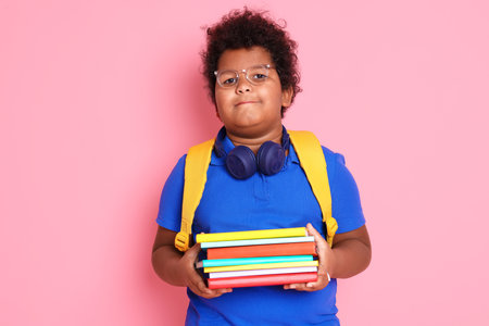 Cute little boy with headphones, notebooks and backpack on pink backgroundの写真素材