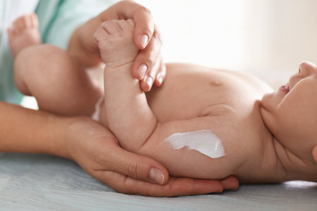 Mother applying cream onto her baby's arm on changing table at home, closeupの写真素材
