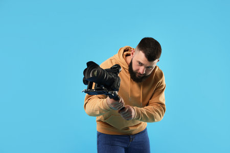 Videographer using gimbal stabilizer with camera on light blue background. Space for textの写真素材