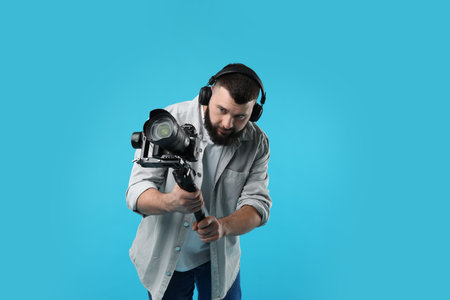 Videographer using gimbal stabilizer with camera on light blue backgroundの写真素材