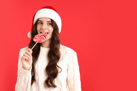 Smiling woman in Santa hat with lollipop on red background, space for text. Merry Christmas and Happy New Yearの写真素材