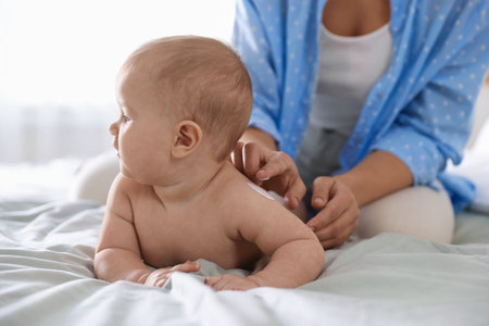 Mother applying cream onto her baby's arm on bed at home, closeupの写真素材