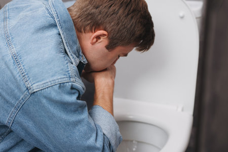 Young man suffering from nausea over toilet bowl in bathroomの写真素材