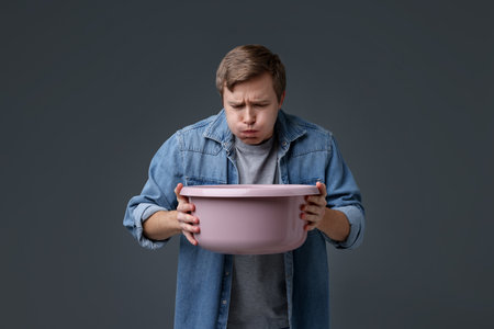 Young man with basin suffering from nausea on gray backgroundの写真素材
