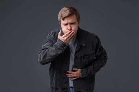 Young man suffering from nausea and stomachache on gray backgroundの写真素材