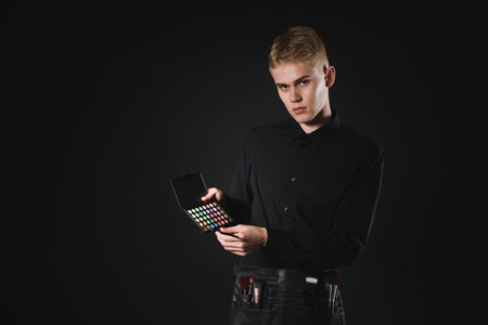 Makeup artist with eyeshadow palette and set of brushes on black background. Space for text