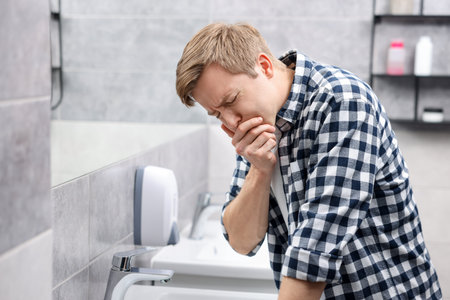 Young man suffering from nausea over sink in bathroomの写真素材