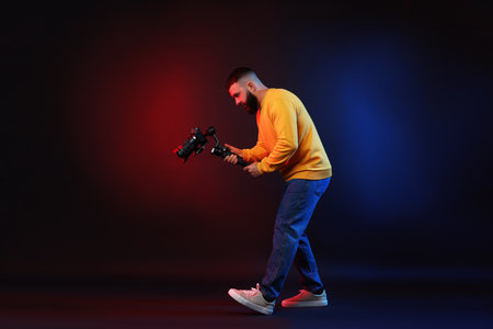 Videographer filming on camera using gimbal stabilizer against dark background with color lights