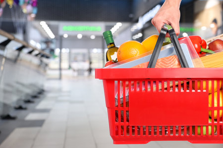 Customer holding shopping basket with different food products at supermarket, closeupの写真素材