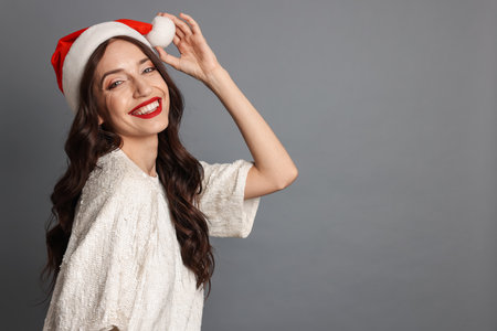 Portrait of beautiful woman with Santa hat on gray background, space for text. Christmas seasonの写真素材