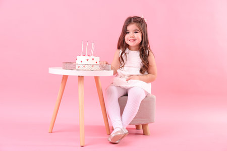 Birthday celebration. Cute little girl and tasty cake on table against pink backgroundの写真素材