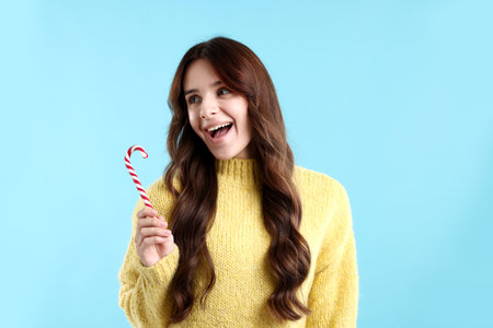 Young woman in sweater with candy cane on light blue background. Merry Christmas and Happy New Yearの写真素材