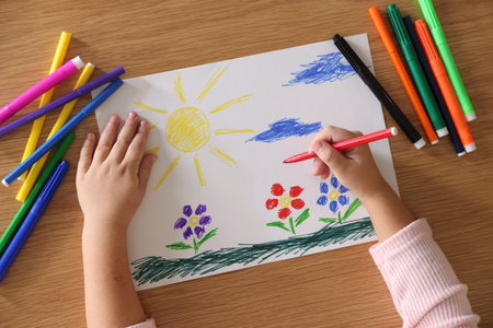 Cute little girl drawing with felt pen at wooden table, top view