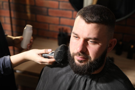 Hairstylist applying talcum powder with brush onto man's beard at salon, closeupの写真素材