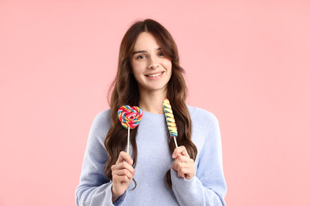 Portrait of smiling woman in sweater with lollipops on pink background.の写真素材