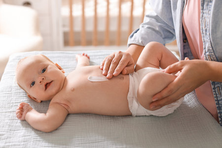 Mother applying cream onto baby's skin on changing table at home, closeupの写真素材