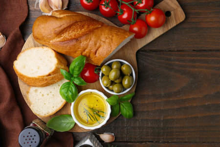 Tasty baguette served with oil, tomatoes, olives and basil on wooden table, flat lay. Space for textの写真素材