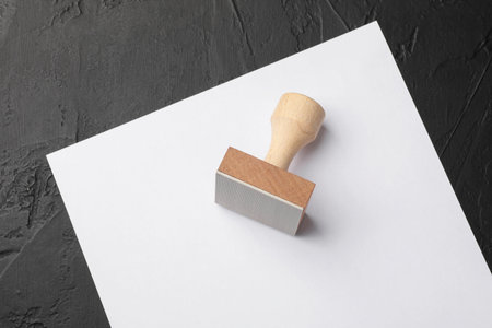 One wooden stamp and blank sheet of paper on dark textured table, top view. Space for textの写真素材
