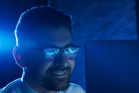 Smiling man wearing glasses with reflection in dark room, closeup