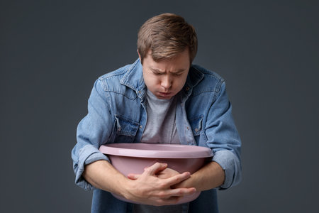 Young man with basin suffering from nausea on gray backgroundの写真素材