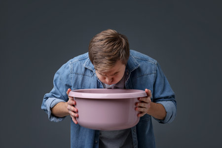 Young man with basin suffering from nausea on gray backgroundの写真素材