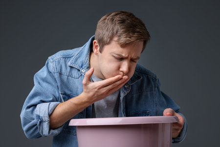 Young man with basin suffering from nausea on gray backgroundの写真素材