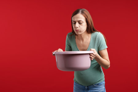 Pregnant woman with basin suffering from nausea on red background. Space for textの写真素材