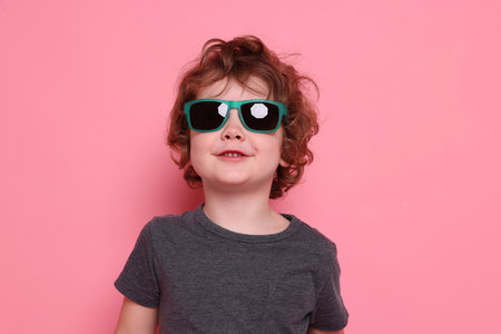Cute little boy in sunglasses on pink background