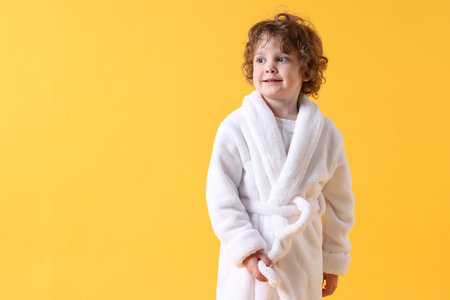 Cute little boy in white bathrobe on yellow background. Space for textの写真素材