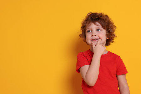 Portrait of cute little boy on orange background, space for textの写真素材