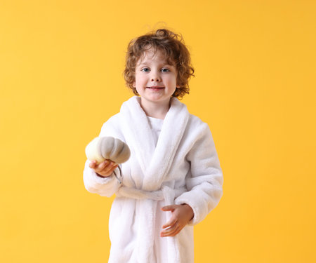 Portrait of smiling little boy in white bathrobe with washcloth on yellow backgroundの写真素材