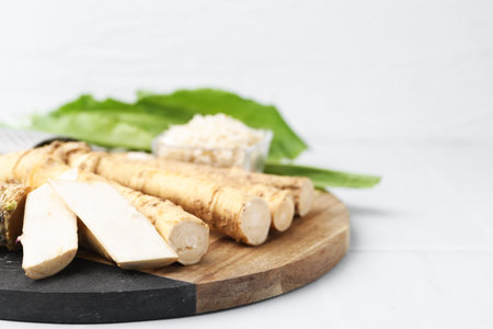 Whole and grated horseradish roots and green leaves on white table, closeup. Space for textの写真素材