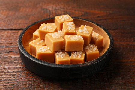 Tasty caramel candies with salt in bowl on wooden table, closeupの写真素材