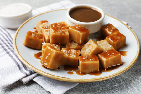 Tasty candies with salt and caramel sauce on gray textured table, closeupの写真素材