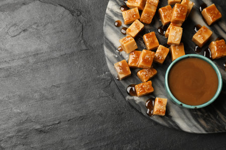 Tasty candies with salt and caramel sauce on dark textured table, top view. Space for textの写真素材
