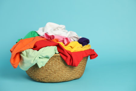 Wicker basket with laundry on light blue background, closeup. Space for textの写真素材