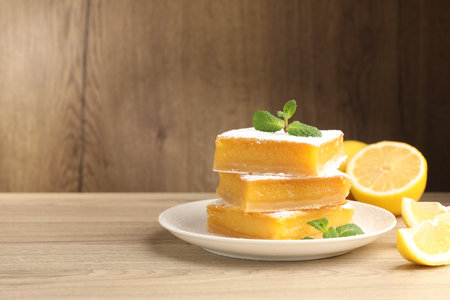 Tasty lemon bars with mint and fresh fruits on wooden table, closeup. Space for textの写真素材