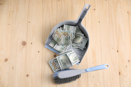 Dustpan with broom and dollar banknotes on wooden background, flat layの写真素材