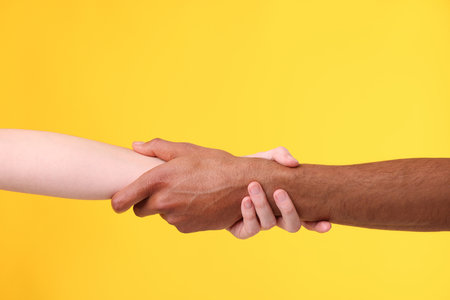 African American man joining hands with his partner on yellow background, closeupの写真素材
