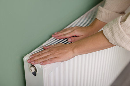 Woman warming her hand near radiator indoors, closeup