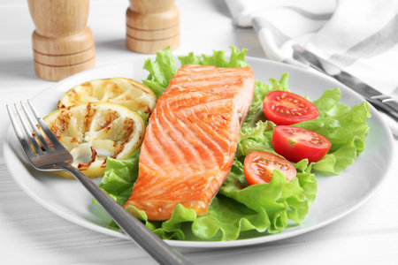 Piece of tasty grilled salmon, lemon slices and salad on white wooden table, closeupの写真素材