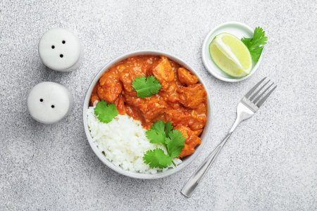 Delicious chicken tikka masala with rice, cilantro, lime and spices served on gray textured table, flat layの写真素材