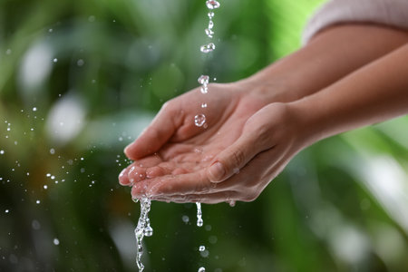 Woman splashing water on blurred green background, closeup