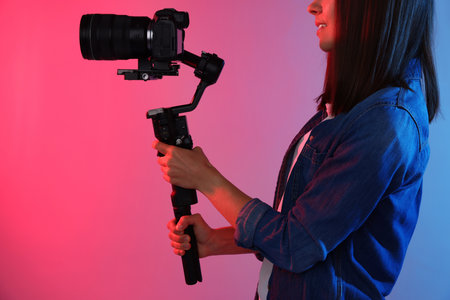 Videographer filming on camera using gimbal stabilizer against background with color lights, closeup
