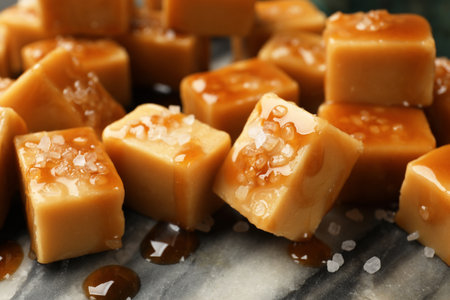 Tasty candies with salt and caramel sauce on dark marble table, closeupの写真素材
