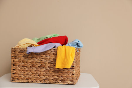 Wicker basket with laundry on white table near beige wall indoors, space for textの写真素材
