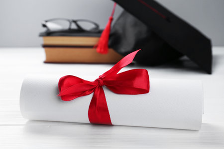 Graduation cap, diploma, glasses and books on white wooden table against light background, selective focusの写真素材