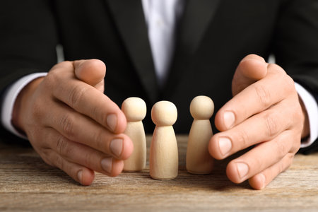 Man protecting human figures at wooden table, closeupの写真素材